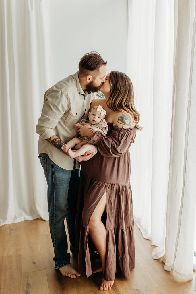 Couple kisses while holding their baby Vancouver Washington Family photographer