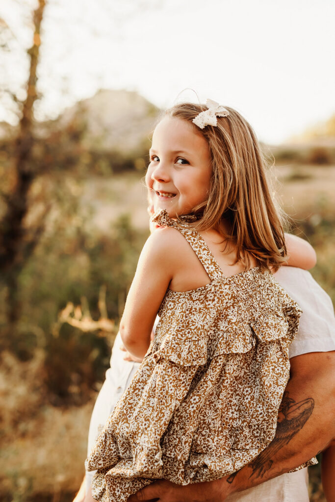 A llittle girl smiles happily at the camera, from the safety of her dad's arms. As captured by a Vancouver Washington Photographer who focuses on capturing authentic moments.