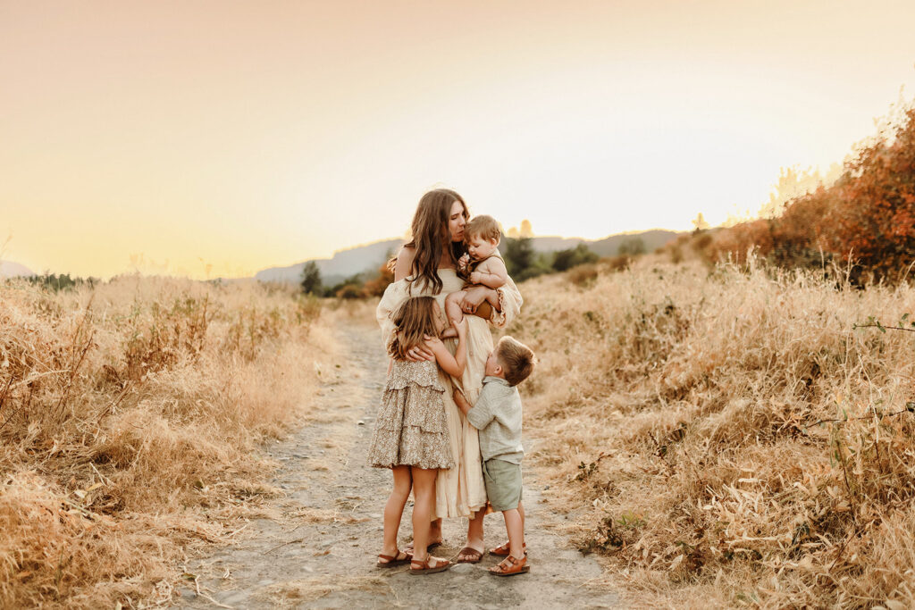 A mom stands snuggling with her three young children as captured by a Vancouver Washington Photographer who focuses on capturing authentic moments.