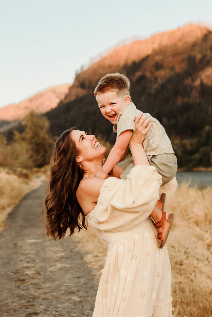 A mom holds her son up above her in as she hoists him up into the air. They are both laughing, as she looks to him in admiration. A joyful and candid connection captured by a photographer who specializes in capturing connection.