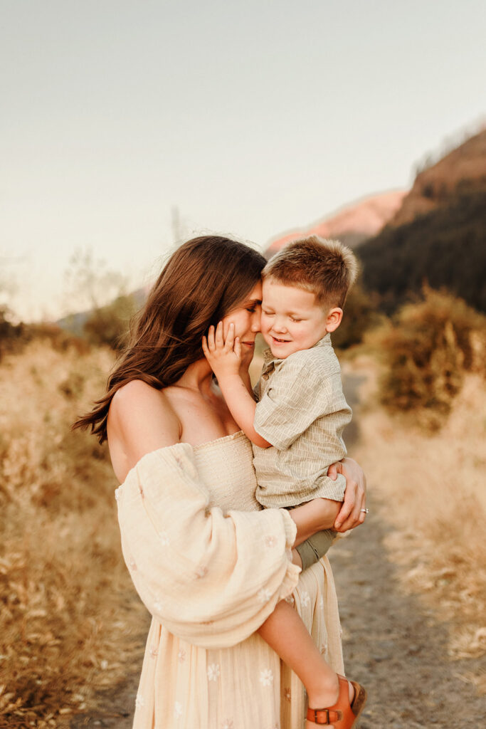 A mom holds her small child and nuzzles her face to him, as he smiles with eyes closed and holds her face tenderly - as captured by a Vancouver Washington Photographer who focuses on capturing authentic moments.