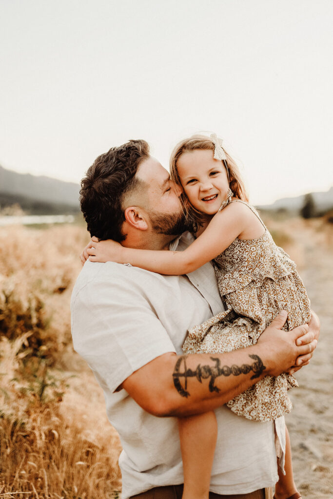 A dad holds his daughter, hugs her and whispers a secret in her ear as captured by a Vancouver Washington Photographer who focuses on capturing authentic moments.
