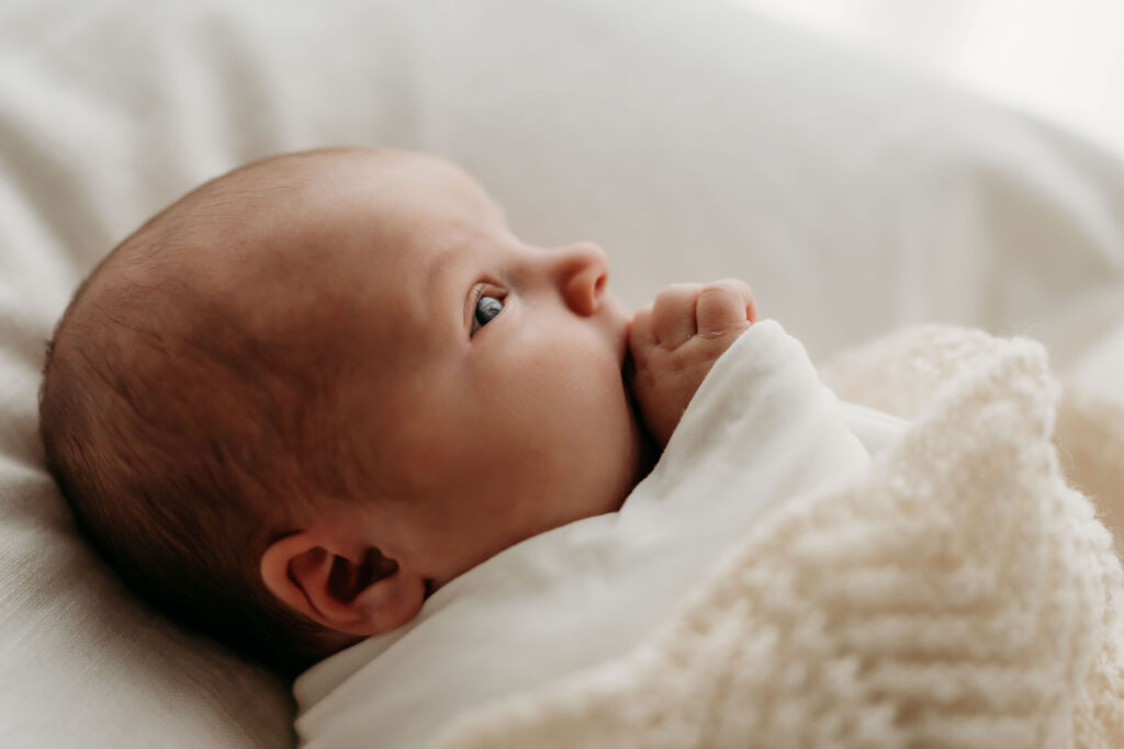 A newborn baby lays sweetly swaddled in soft knits, looking upwards with eyes full of wonder in a Vancouver WA area newborn photography studio. The image shows the wonder and magic of the fleeting newborn stage.
