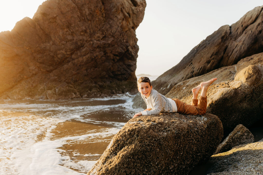  A child plays on the rugged oregon coast with waves and golden hour light in the background during an Oregon Coast family photography session
