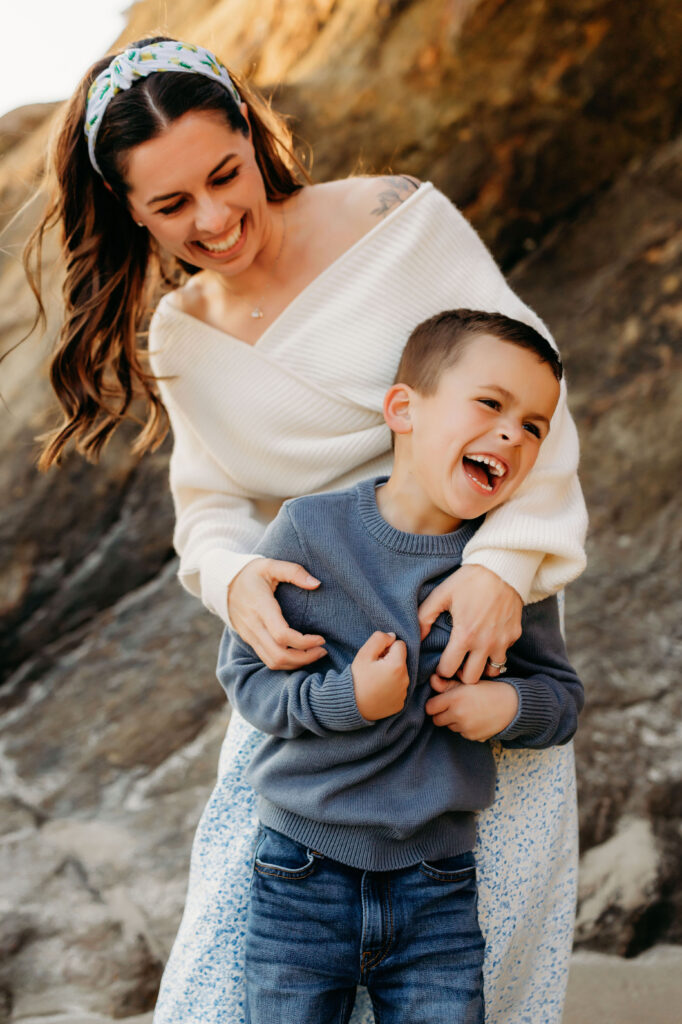 relaxed portrait of Mom and child giggling together as they enjoy taking in the Oregon coast during their family photoshoot.