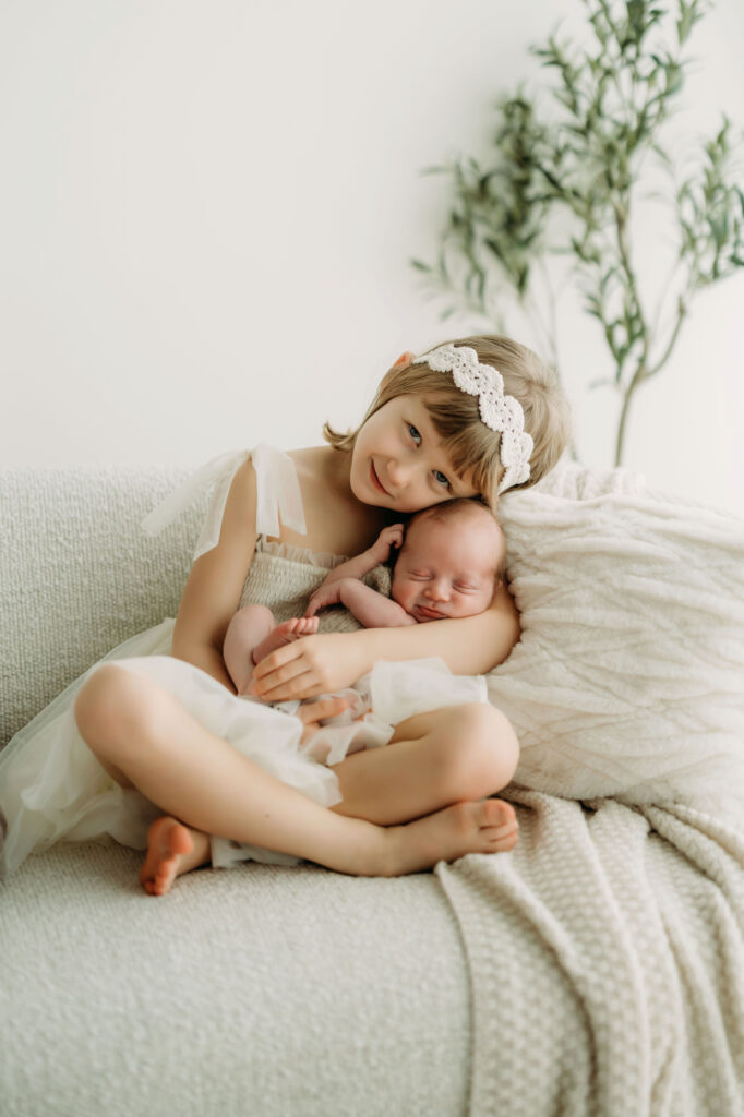 Studio newborn photography session in Vancouver, Washington featuring a wrapped newborn baby being held and snuggled by big sister